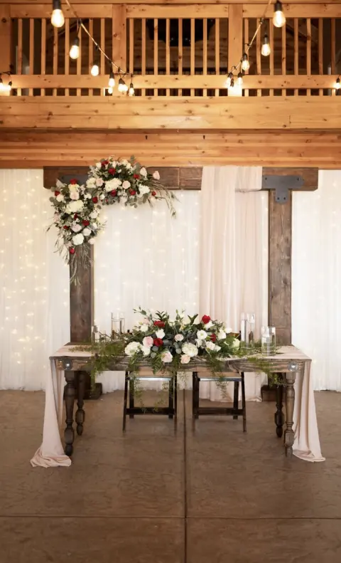 Rustic sweetheart table with floral arrangements and a wood backdrop